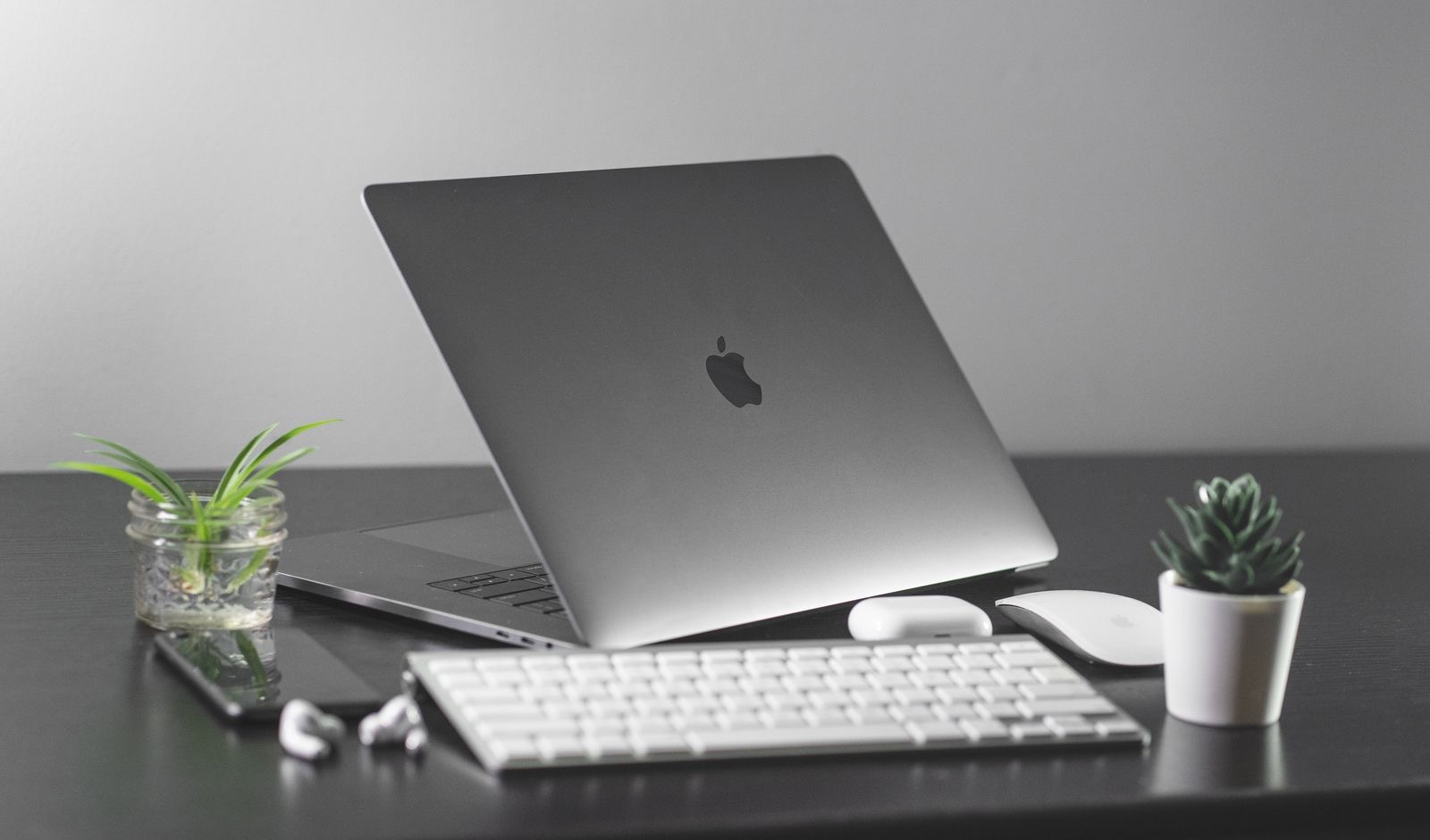 A minimalist Mac desk with a laptop, keyboard, and a small plant on a warm wooden surface.