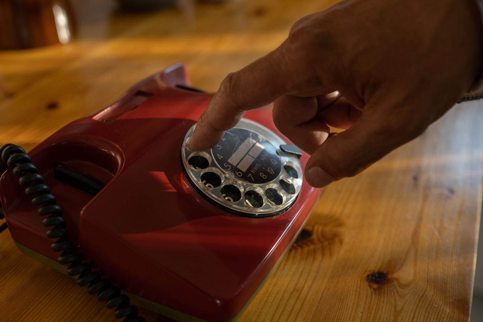 A finger dialing a number on a red rotary telephone on a wooden table - the original speed dial.