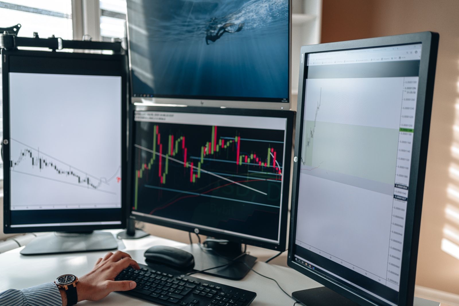 Someone typing at a multi-monitor desk filled with financial charts and market data - the keyboard-driven world where shortcuts win.