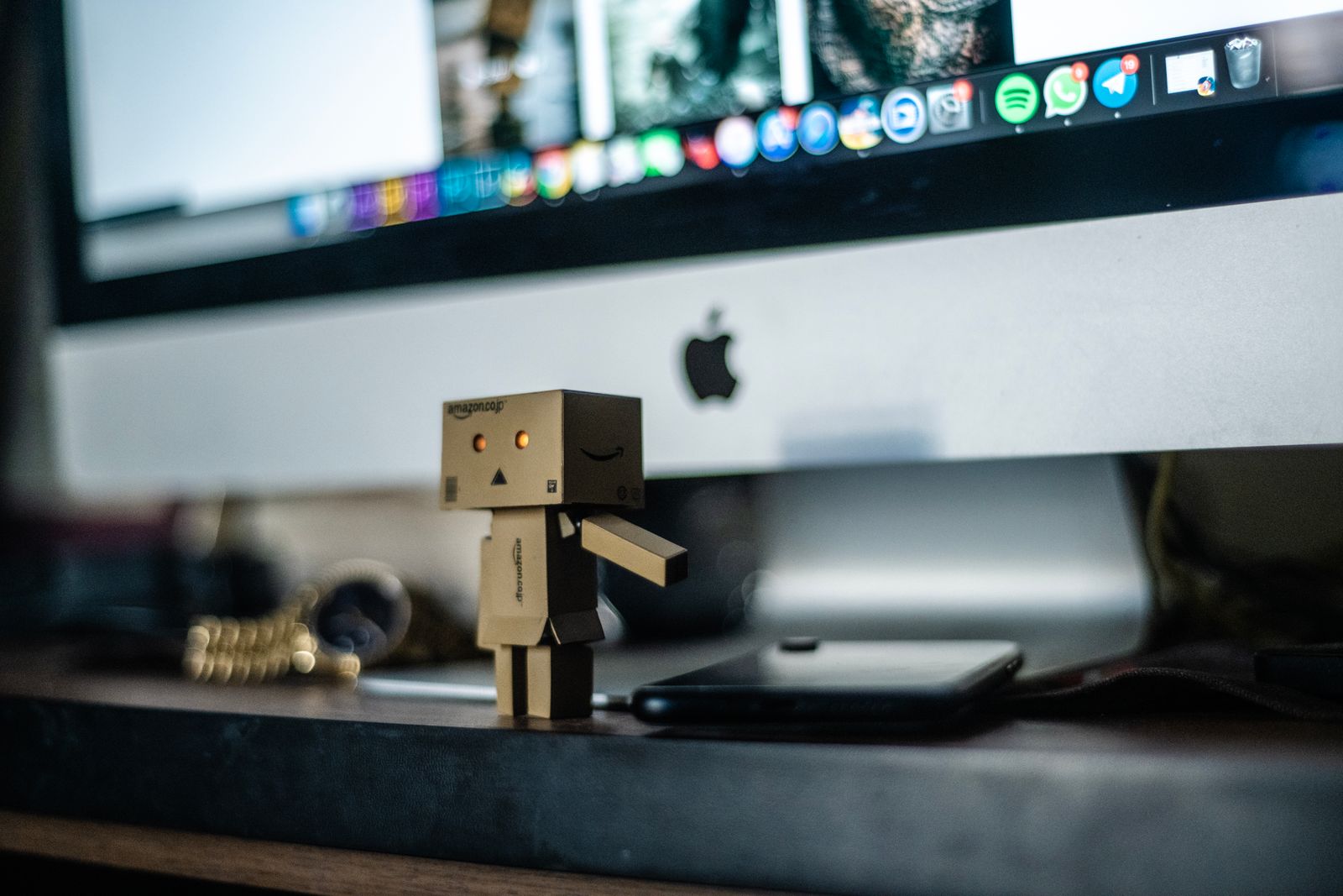 A small cardboard robot sitting in front of a computer screen on a desk - a playful take on telling your computer what to do.