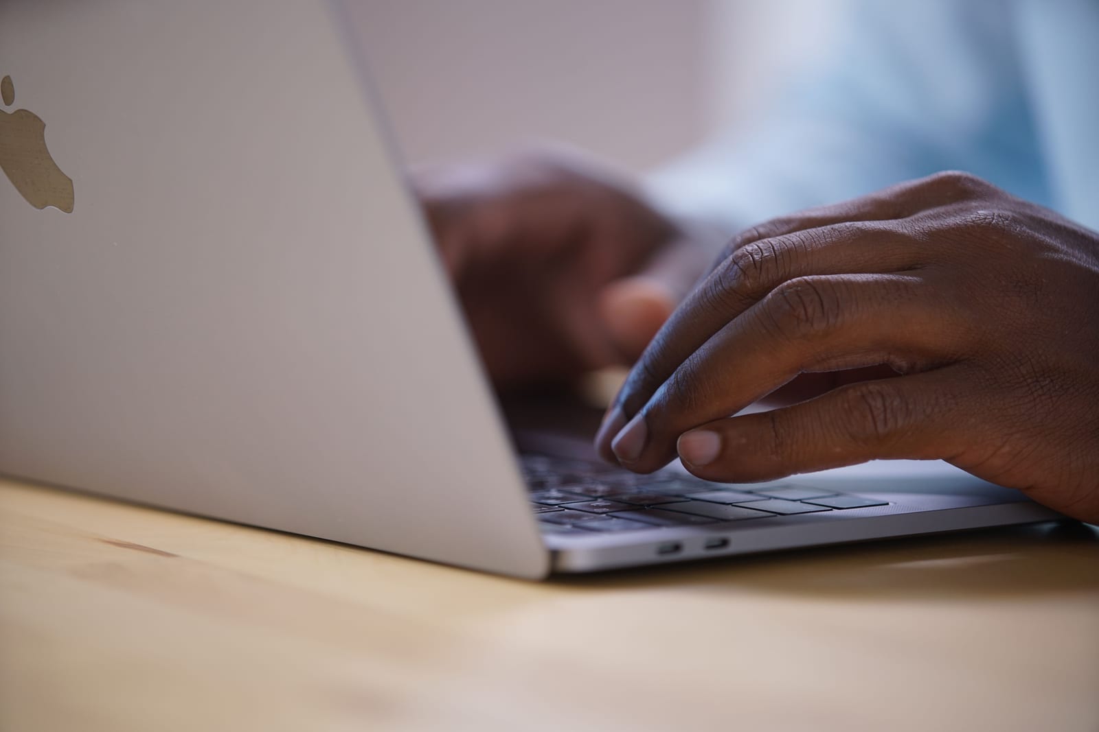 Close-up of hands mid-keystroke on a MacBook keyboard at a wooden desk - pressing the key combination you want to assign.