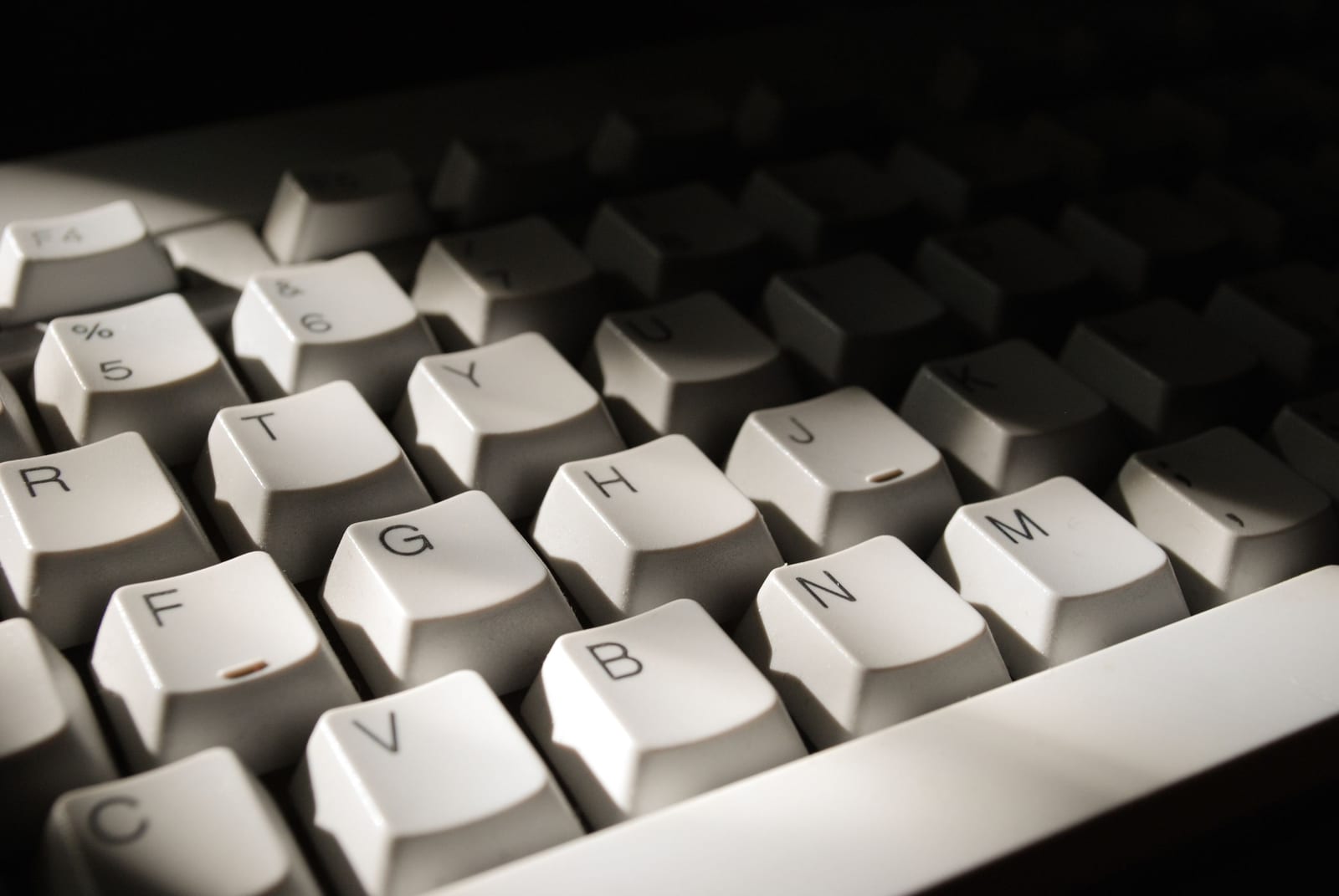 A keyboard lit from one side, its keys receding into shadow - a shortcut that has stopped working without any visible reason.