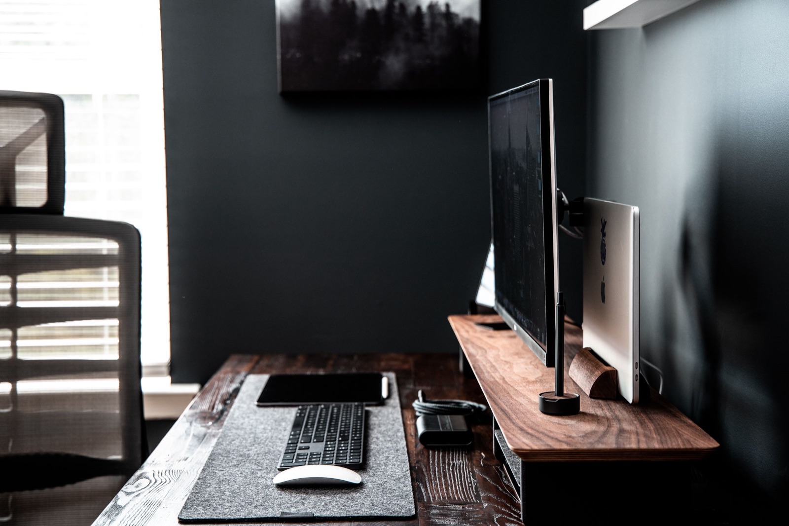 A single monitor on a wooden riser above a keyboard and mouse in a dark, tidy home office - a Mac workspace set up to run itself with the built-in tools.