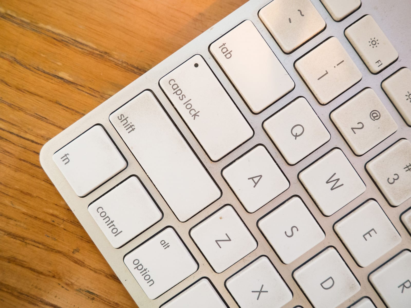 A white Apple keyboard on a warm wooden desk, angled so the fn, control, option, shift and caps lock keys are all readable - the modifier keys this guide decodes.