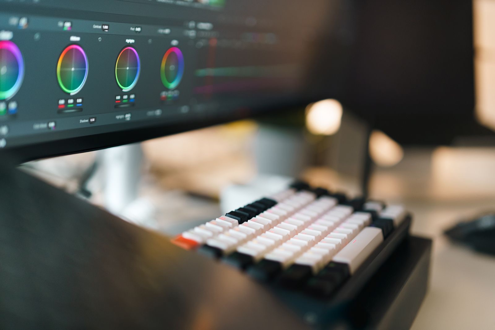 A mechanical keyboard in front of a monitor running color-grading software - keyboard fluency in a complex creative app.